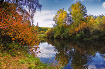 Autumn river with reflecting trees against the backdrop of forests and mountains.