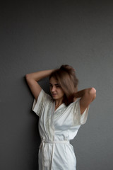 Fototapeta premium A young, beautiful girl in a robe is touching her brown hair. The girl's look is directed a little aside. Around the girl is a gray background and a space for text or graphics.