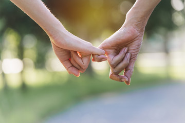 Closeup two person hook each other's little finger on nature background.