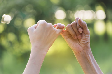 Closeup two person hook each other's little finger on nature background.
