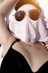 A girl with glasses sunbathes in the sun. The girl's face is covered with a towel