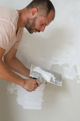 Man plastering wall with putty-knife. Fixing wall surface and preparation for painting. DIY housing improvement project.
