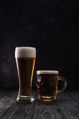 glass and mug of fresh light beer with foam on wooden table