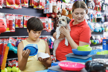 Preteen boy with woman and little dog buying pet supplies in shop