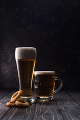 glass and mug of fresh light beer near fried onion rings on wooden table