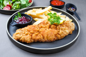 Fried Wiener schnitzel from veal topside with French fries and lettuce as closeup modern design...