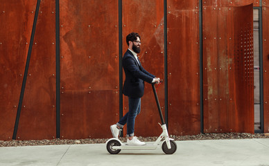 Bearded man riding electric scooter on sidewalk