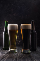 glasses of fresh light and dark beer near bottles on wooden table