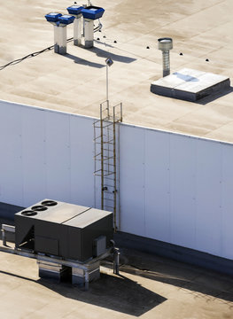 Roof of a commercial building with a external units of the commercial air conditioning and ventilation systems and a metal staircase.