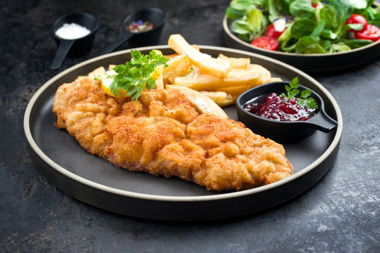 Frittiertes Wiener Schnitzel von der Oberschale vom Kalb mit Pommes Frites und Salat als closeup auf einem Modern Design Teller