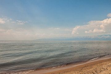 Russia. Lake Baikal. Barguzinsky Bay. Summer sandy beach on a background of mountains and a blue sky with clouds.