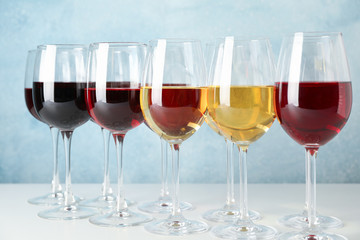 Glasses with different wine on white table against light blue background