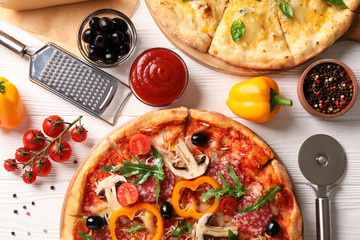 Delicious pizza and ingredients on white wooden background, top view