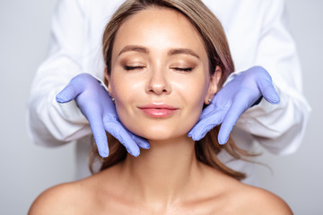 Close up portrait of young blonde woman with cosmetologyst hands in a gloves. Preparation for...