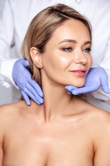 Close up portrait of young blonde woman with cosmetologyst hands in a gloves. Preparation for operation or procedure. Perfect skin, spa and care