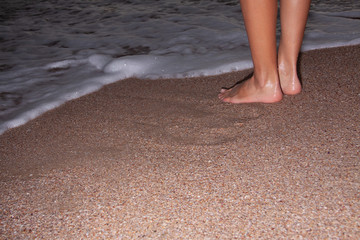 Close-up of female legs at the beach in the evening. Girl walking on the beach at night.