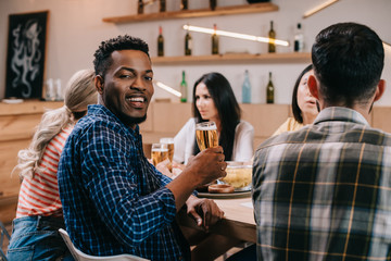 handsome african american man looking at camera while sitting in pub with friends