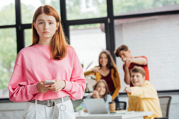 group of schoolchildren bullying sad girl with smartphone