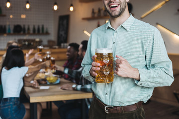 cropped view of smiling young man holding mug of light beer in pub