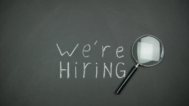 Magnifier moves over black background. The inscription 'we're hiring" written in chalk. Stop motion