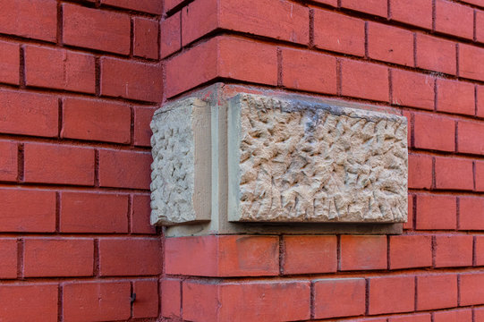 Helle Bossensteine aus Sandstein als Ecksteine in Farbkontrast zu einer Hauswand mit Wandversatz aus rotem Ziegelstein mit kleinen Steinen und breiten, tiefen Fugen aus Putz hergestellt
