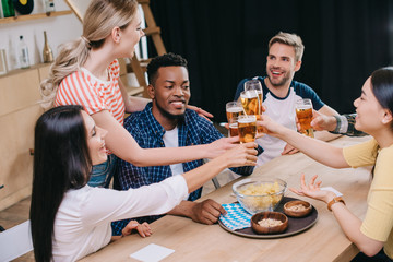 cheerful multicultural friends clinking glasses of light beer in pub