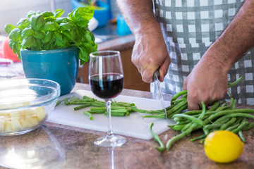 Close up of man working at home in the kitchen cutting at home some healthy beans food - chef or husband people working - red cup of wine on the table