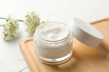 Fototapeta na wymiar Jar with cream, allium flowers and board on white background, closeup