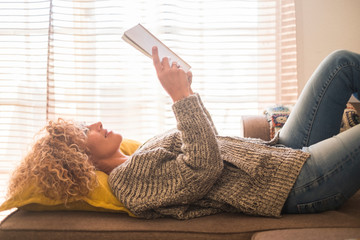 Adult relaxed beautiful curly blonde hair caucasian woman lay down and read a paper book alone at...