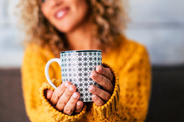 Close up of design trendy mug with tea or coffee or heahty drink holded by adult caucasian woman hands -  cheerful blonde female people in background defocused