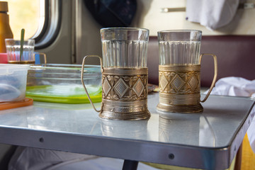 Empty glasses in metal cup holders stand on a table in a train compartment