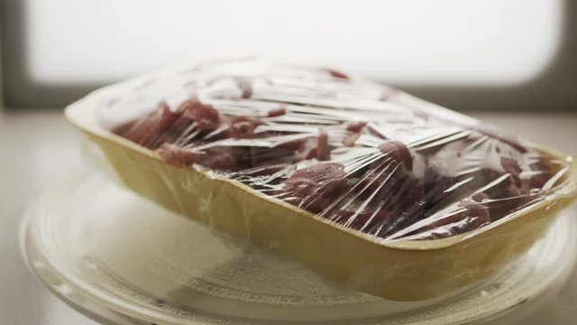 Fresh raw сhicken offal in food tray with plastic wrap rotating in microwave.