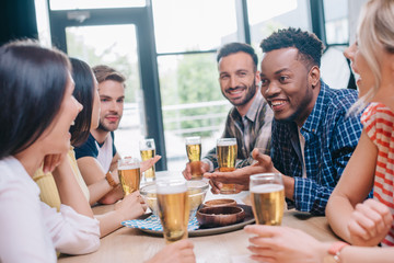 cheerful multicultural friends talking while sitting together in pub