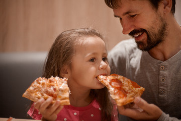 father feeding his cute daughter with pizza