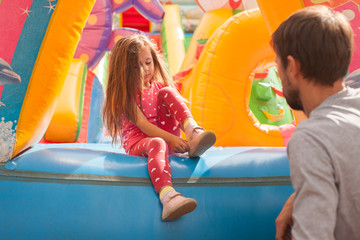 Fototapeta na wymiar Dad puts shoes on a little girl playing on a inflatable castle
