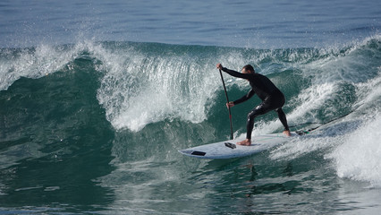 Paddle boarder in wetsuit on huge wave