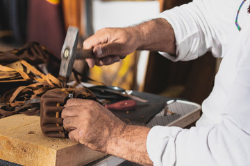 Man with hammer in hand working on leather sandals, homemade concept