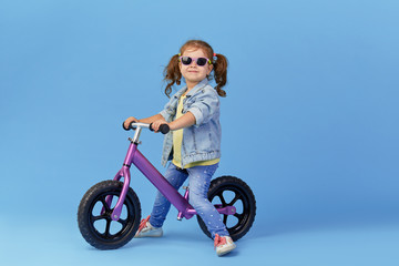 Little girl learns to keep balance while riding a bicycle. Stylish child in sunglasses  isolated on...