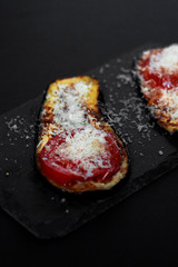 Slices of grilled eggplant with tomato and cheese on black stone board on black background. Close up.