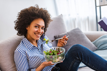 Beautiful young woman having a fresh healthy meal in the living room. Smiling young woman eating...