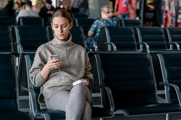 Fototapeta na wymiar Young girl at the airport waiting for her departure. Scrolling smartphone