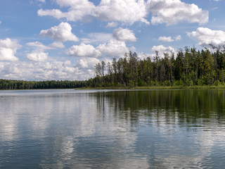 Fototapeta na wymiar Lake shines green in summer under blowing clouds, white clouds of interesting shape reflect on lake surface, Lake Valdis, Turna, Latvia