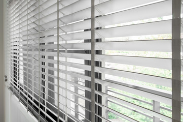Closeup white color wooden blind with white ladder tape curtains.Sunlight through the windows in the city with garden.Selective focus and light image backdrop.