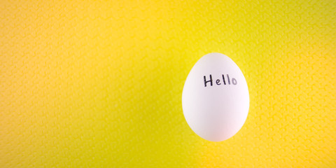 White chicken egg with black inscription hello on a yellow background.