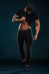 Strong and fit man bodybuilder shows abdominal muscles under a t-shirt. Sporty muscular guy athlete. Sport and fitness concept. Men's fashion.