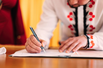 the groom holds the pen and puts a signature in the notebook. ce