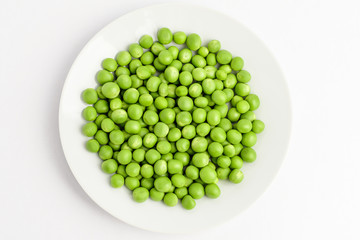 Fresh organic green peas on a round white plate isolated on white, top view, with space for text