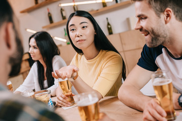 selective focus of young asian woman gesturing while sitting with friends in pub
