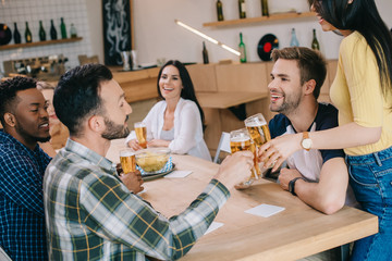 cheerful multicultural friends talking while drinking beer in pub