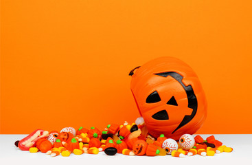 Halloween Jack o Lantern bucket with spilling candy, side view on an orange background